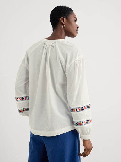 Woman wearing a white blouse with colourful embroidery on sleeves against a white background