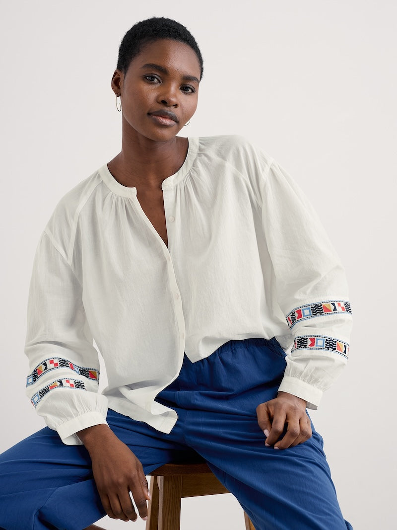 Woman wearing a white blouse with colorful embroidery and blue pants on a white background