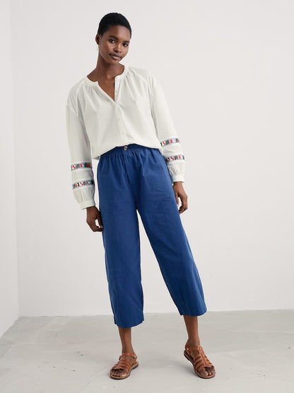 Woman wearing a white blouse with colourful accents and blue pants on a white background
