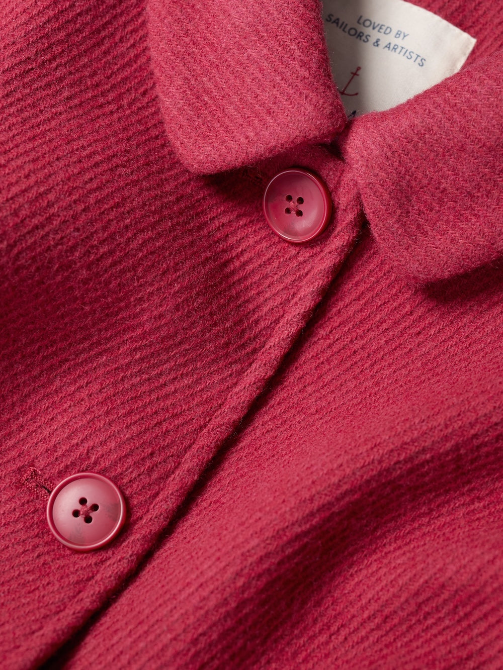 Close-up of a pink textured garment with buttons and a label.