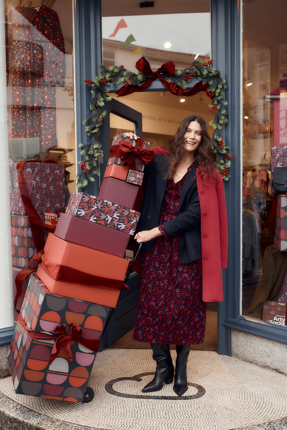 Woman standing in front of a store window with large gift boxes and Christmas decorations.