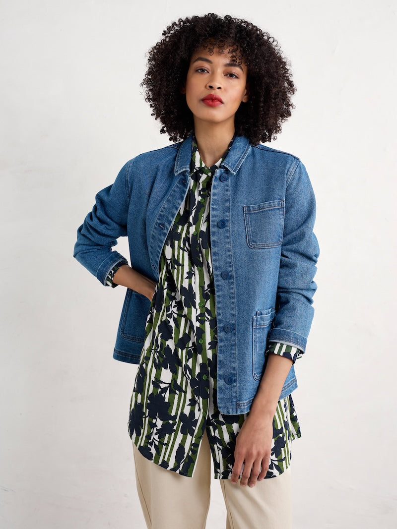 Woman wearing a denim jacket over a patterned shirt on a white background