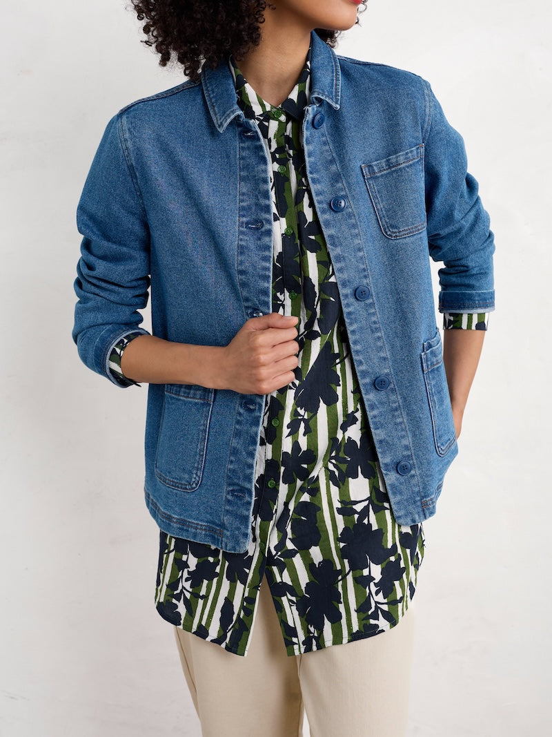 Woman wearing a blue denim jacket over a floral top on a white background