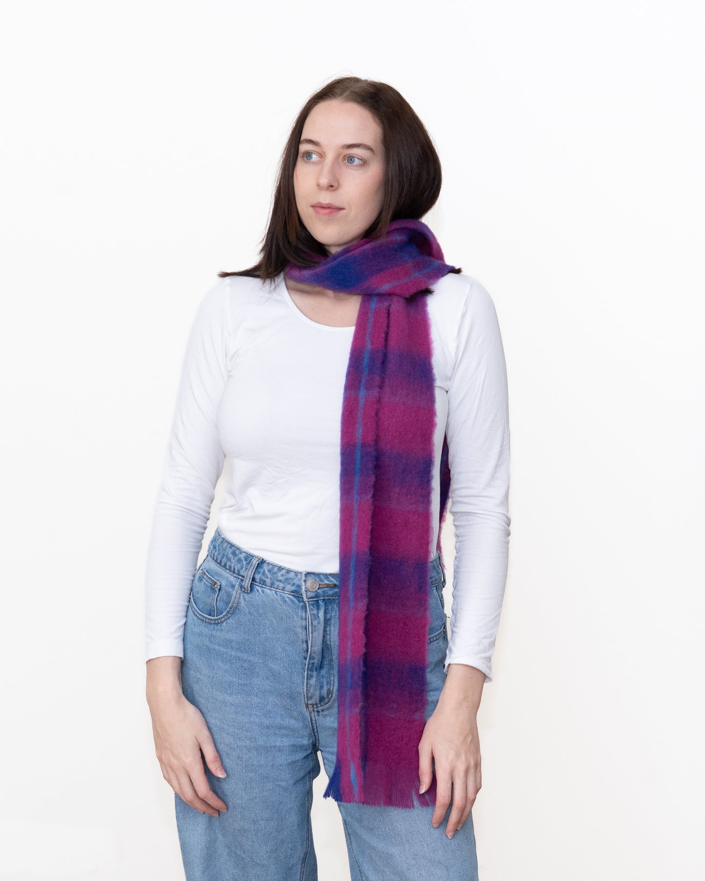 A woman wearing a white long-sleeve top and blue jeans, modeling a lightweight scarf with a purple and blue plaid pattern against a plain white background.