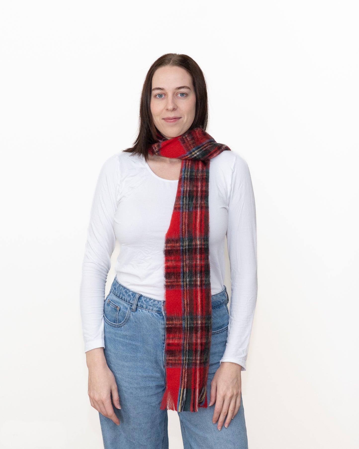 A woman wearing a white long-sleeve top and blue jeans, with a red and black plaid scarf wrapped around her neck, photographed against a plain white background.