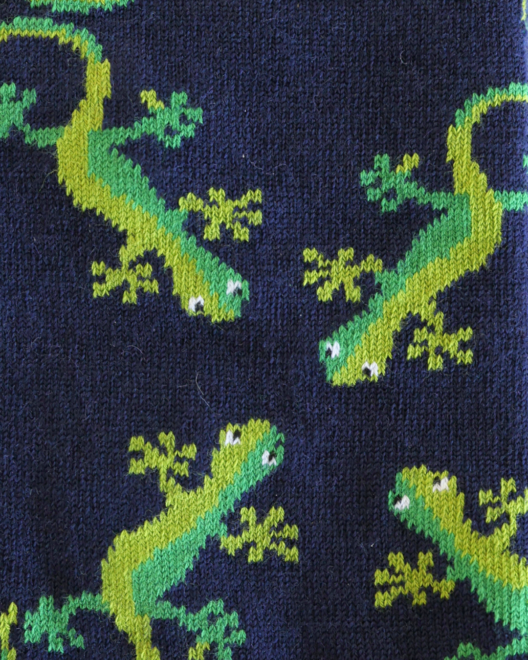 A close-up of a knitted fabric featuring a repeating pattern of bright green lizards on a dark navy blue background.