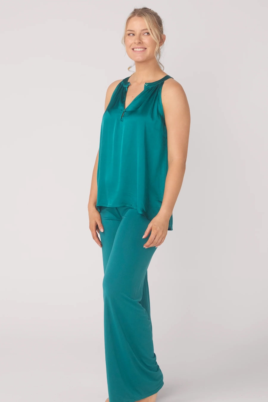 Woman wearing a teal sleeveless top and pants on a white background