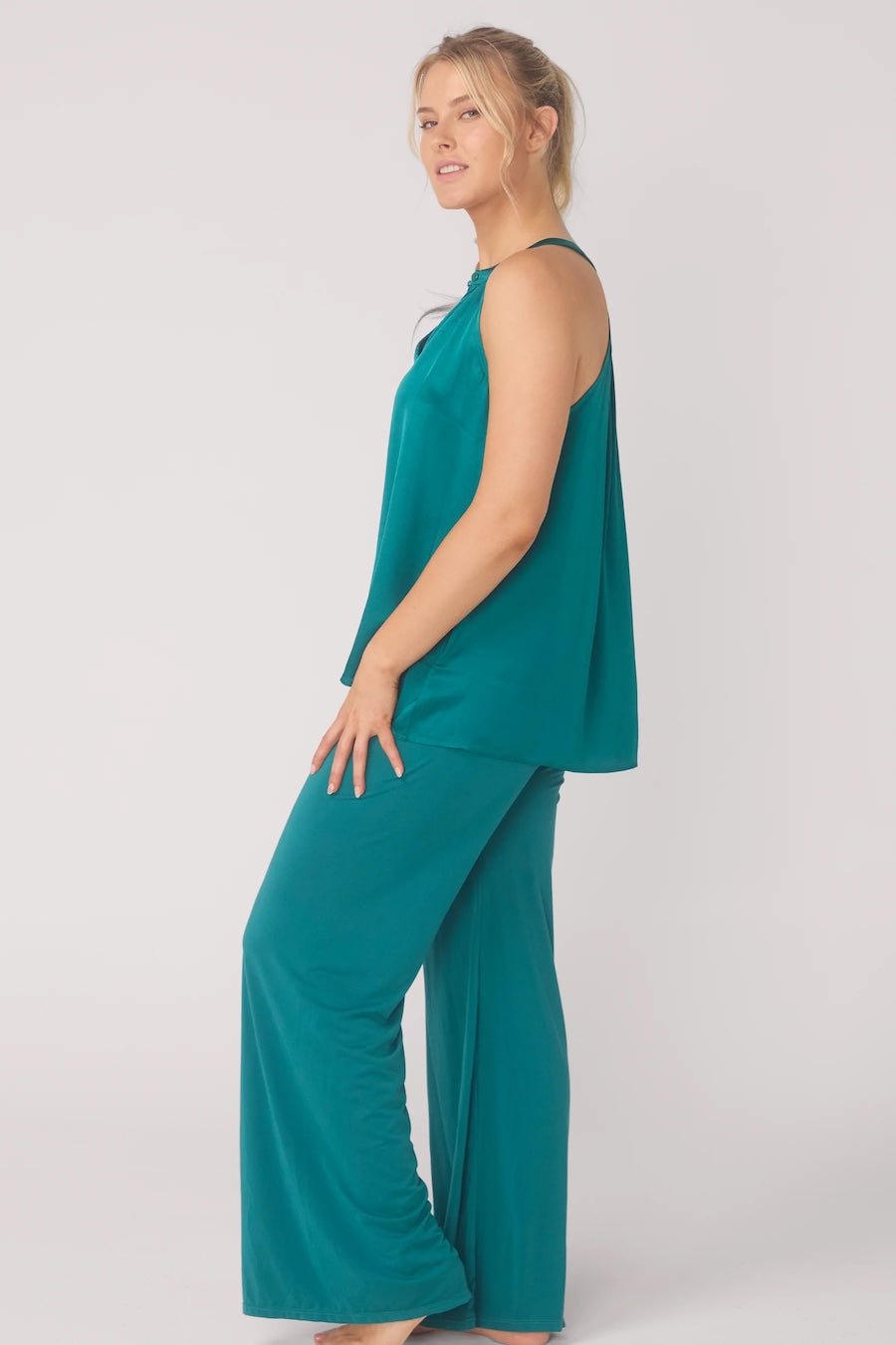 Woman wearing a teal sleeveless top and wide leg pants on a white background