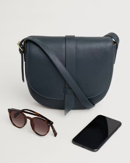 Navy blue leather crossbody bag with sunglasses and phone on a light gray background
