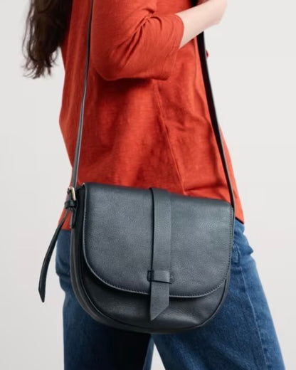 Person wearing a navy crossbody bag with a plain background