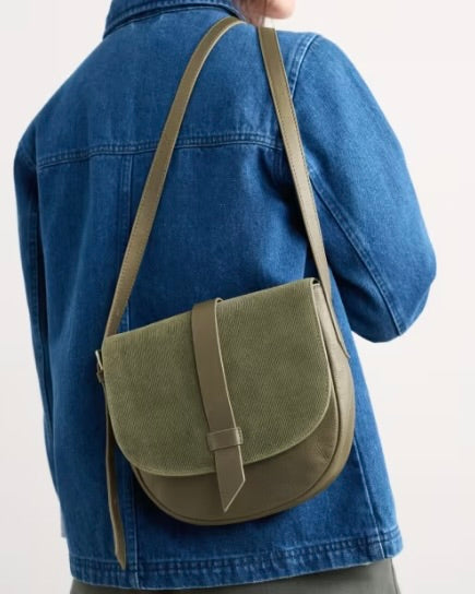 Person wearing a green crossbody bag over a blue denim jacket