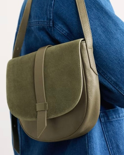 Green shoulder bag worn by a person in a blue jacket on a light gray background