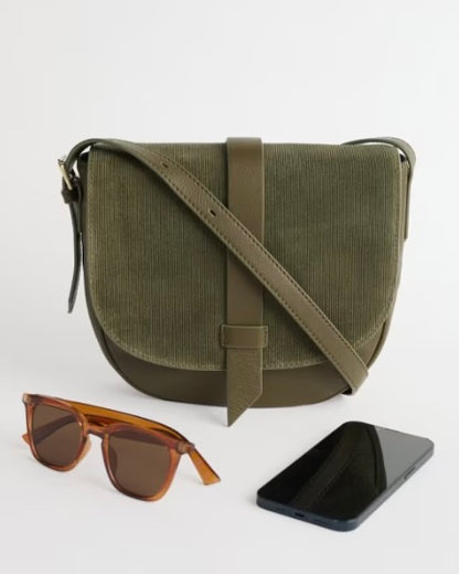Green crossbody bag with sunglasses and phone on a white background