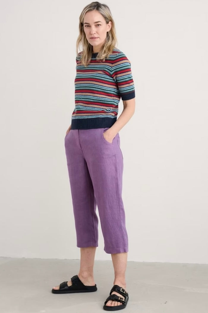 Woman wearing a striped sweater and purple pants against a white background