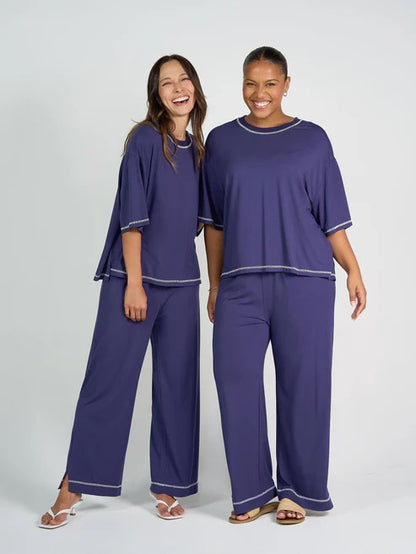 Two women wearing matching blue bamboo shirt and pant sets on a white background