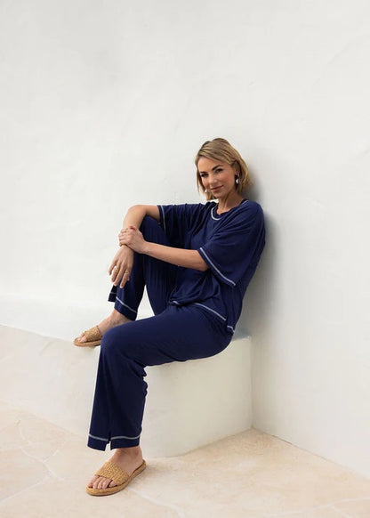 Woman wearing navy blue bamboo shirt and pants sitting against a white wall