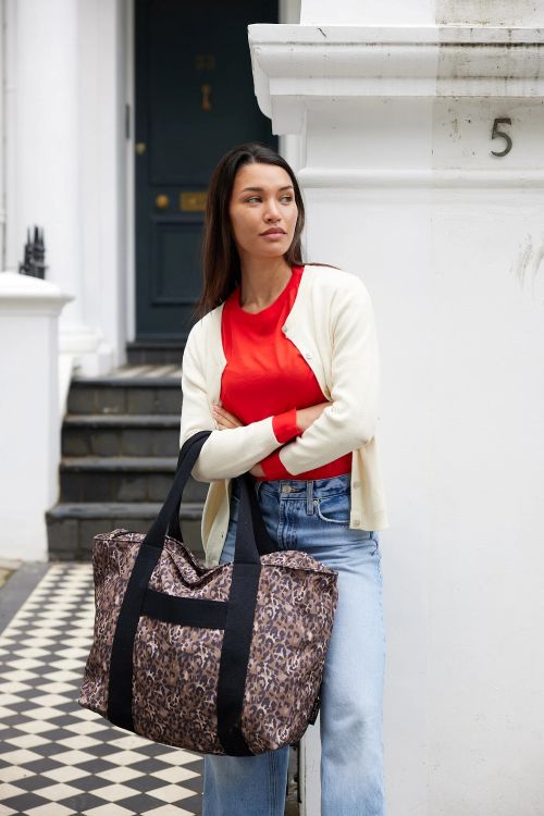 Woman holding a patterned bag in front of a white building.