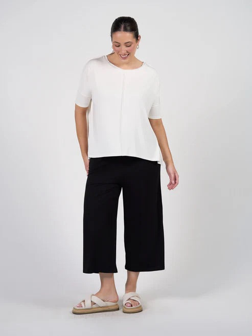Woman wearing a white bamboo top and black bamboo cropped pants on a white background