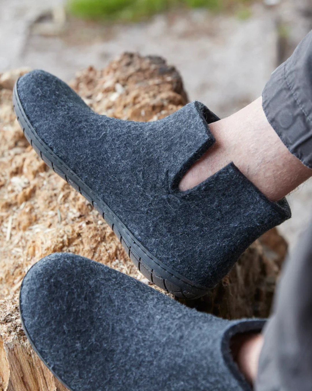Dark gray wool felt ankle boots worn on a person's feet, shown outdoors on a piece of wood with a blurred natural background.