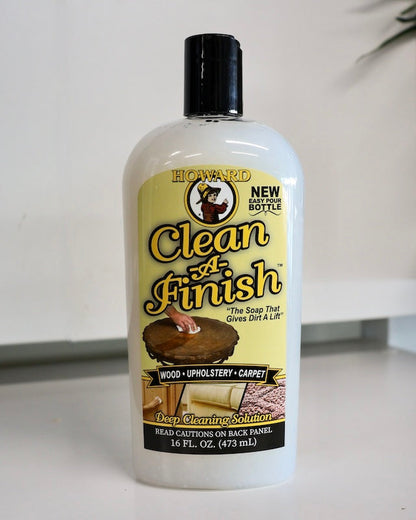 Howard's clean-a-finish wood, upholstery & carpet cleaner in bottle sitting on white bench. Safely cleans wood surfaces. Breaks down dirt & grease on wood surfaces. No harsh detergents, no solvents. 