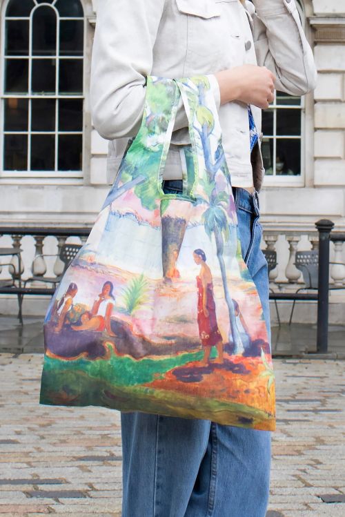Person holding a colourful reusable tote bag with artistic design outdoors.