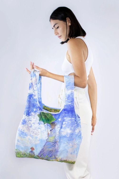 Woman holding a reusable bag with a Monet painting design against a white background