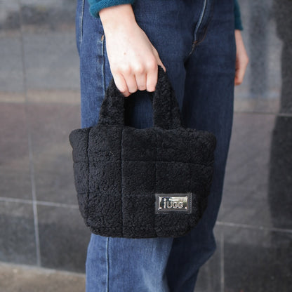 Person holding a black sheepskin handbag with 'UGG' branding against a tiled wall.