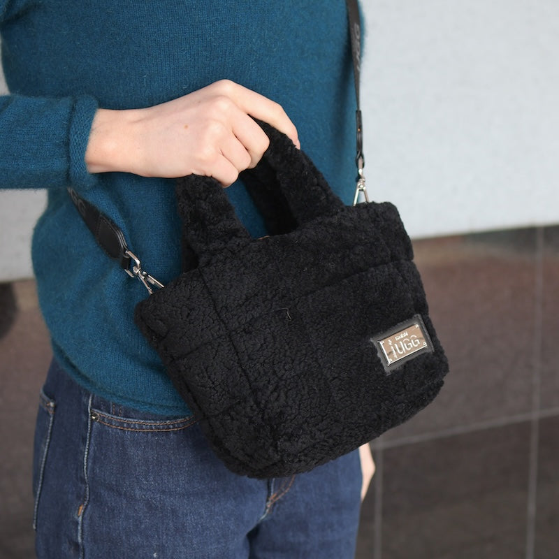 Person holding a black sheepskin handbag with a visible brand logo.