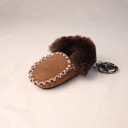 Brown moccasin-shaped keychain with fur trim on a light beige background