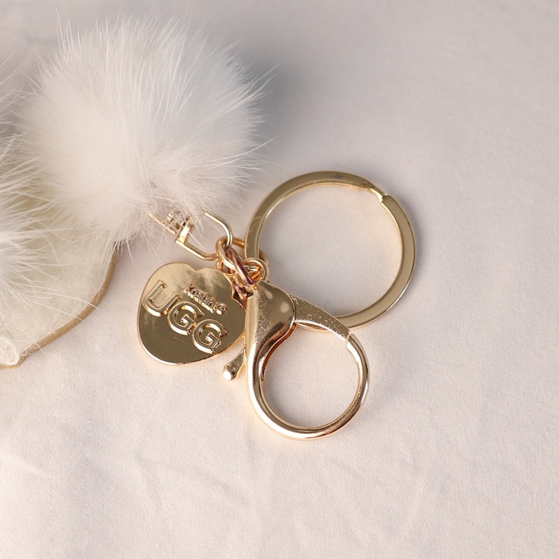 Gold keychain with UGG logo on a soft white background
