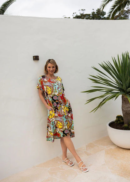 Woman wearing colourful patterned bamboo knee length dress on white background.