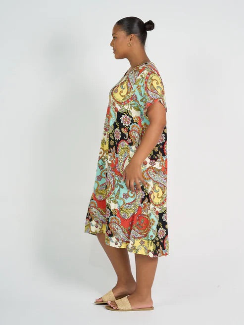 Woman wearing colourful patterned bamboo knee length dress on white background.