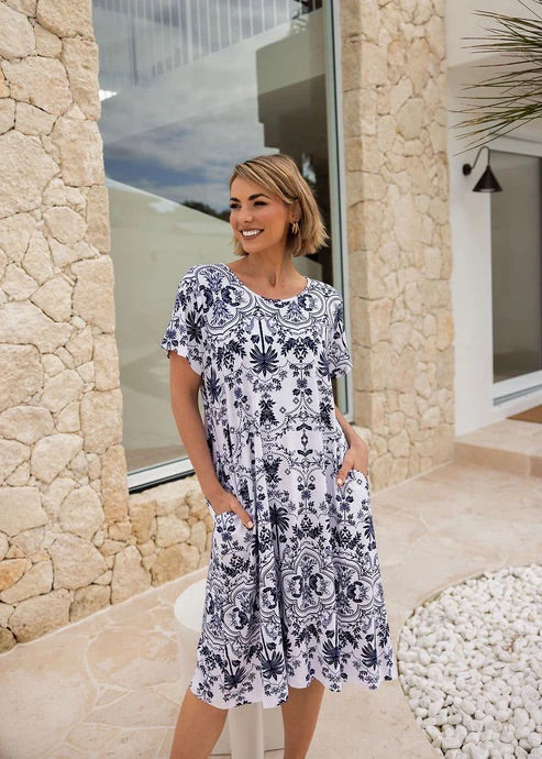 Woman wearing white and blue patterned bamboo knee length dress standing in front of rock wall.