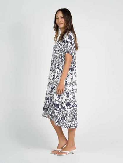 Woman wearing white and blue patterned bamboo knee length dress on white background.