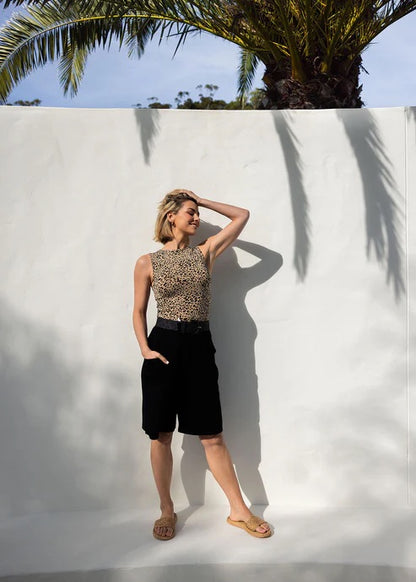 Woman in leopard print top and long black bamboo shorts standing against a white wall with palm tree shadows.