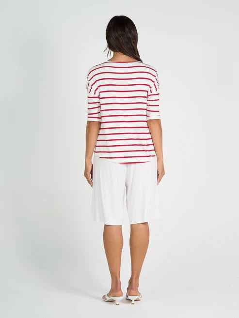 Woman wearing a red and white striped shirt and long white bamboo shorts on a plain background