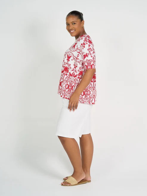 Woman wearing a red and white floral blouse with white long bamboo shorts on a plain background