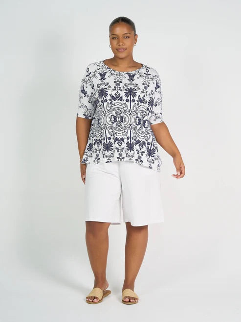 Woman wearing a patterned top and white bamboo shorts on a white background