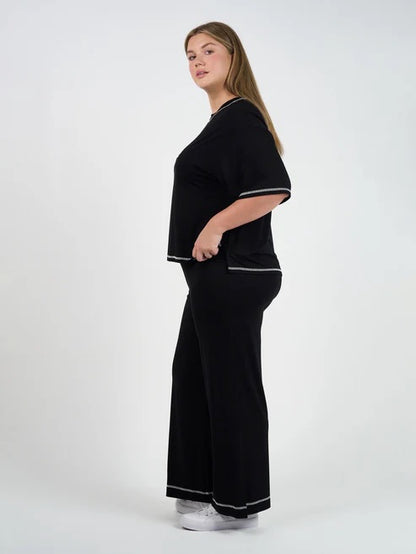 Woman wearing a black bamboo shirt and pants with white trim on a white background