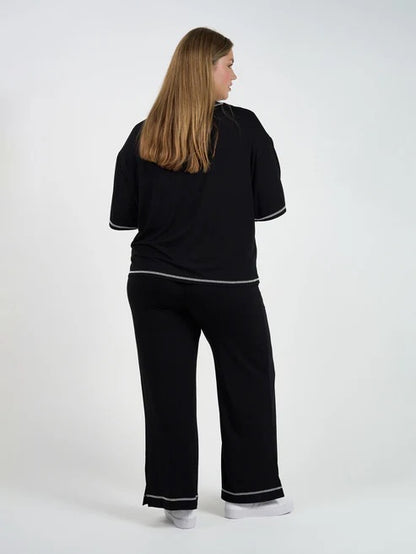 Woman wearing a black bamboo shirt and pants with white trim on a white background