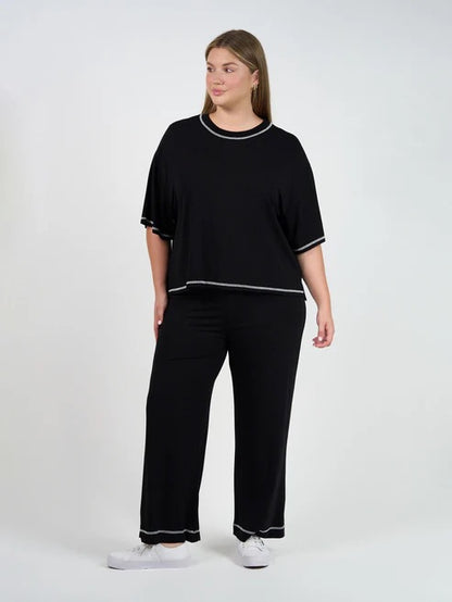 Woman wearing a black bamboo shirt and pants with white trim on a white background