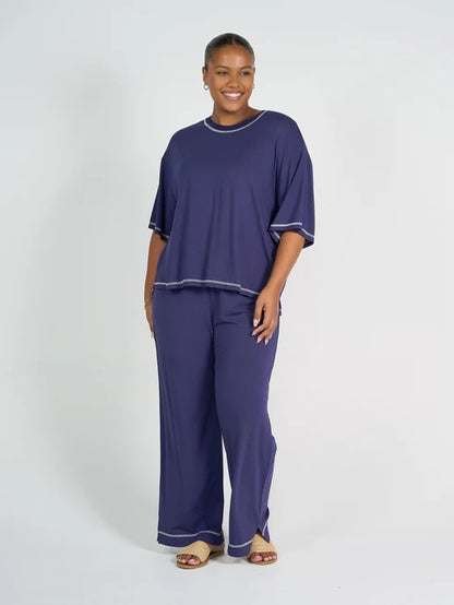 Woman wearing a navy blue bamboo shirt and pants with white trim on a white background