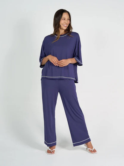 Woman wearing a blue bamboo shirt and pants with white trim on a white background