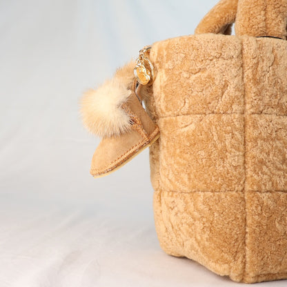 Sheepskin beige handbag with a fluffy pom-pom mini UGG boot keychain on a light grey background