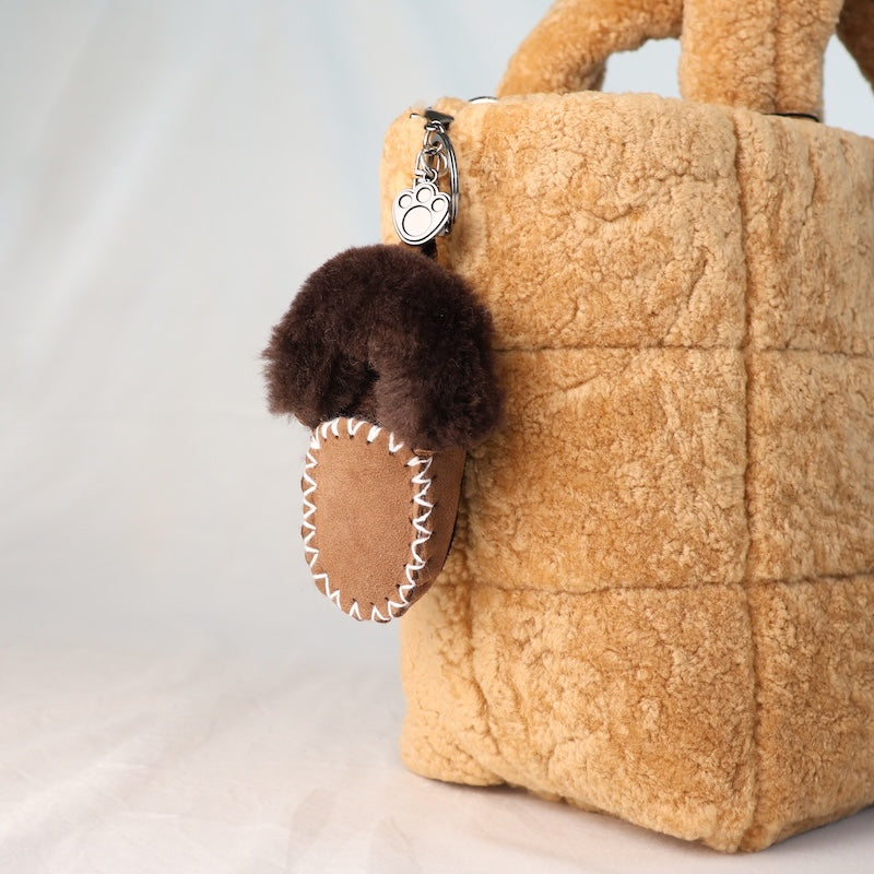 Brown fluffy mini moccasin keychain attached to a beige sheepskin bag on a light grey background