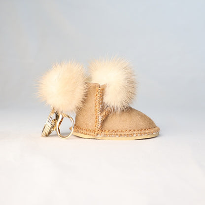 Keychain shaped like a small boot with fur pom-poms on a light grey background