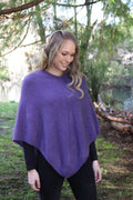 Purple possum and merino wool poncho on female model standing in garden. Warm, soft, lightweight possum and merino wool. Lothlorian