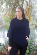 Midnight blue possum and merino wool poncho on female model standing in garden. Warm, soft, lightweight possum and merino wool. Lothlorian