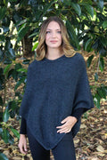 Charcoal grey possum and merino wool poncho on female model standing in garden. Warm, soft, lightweight possum and merino wool. Lothlorian
